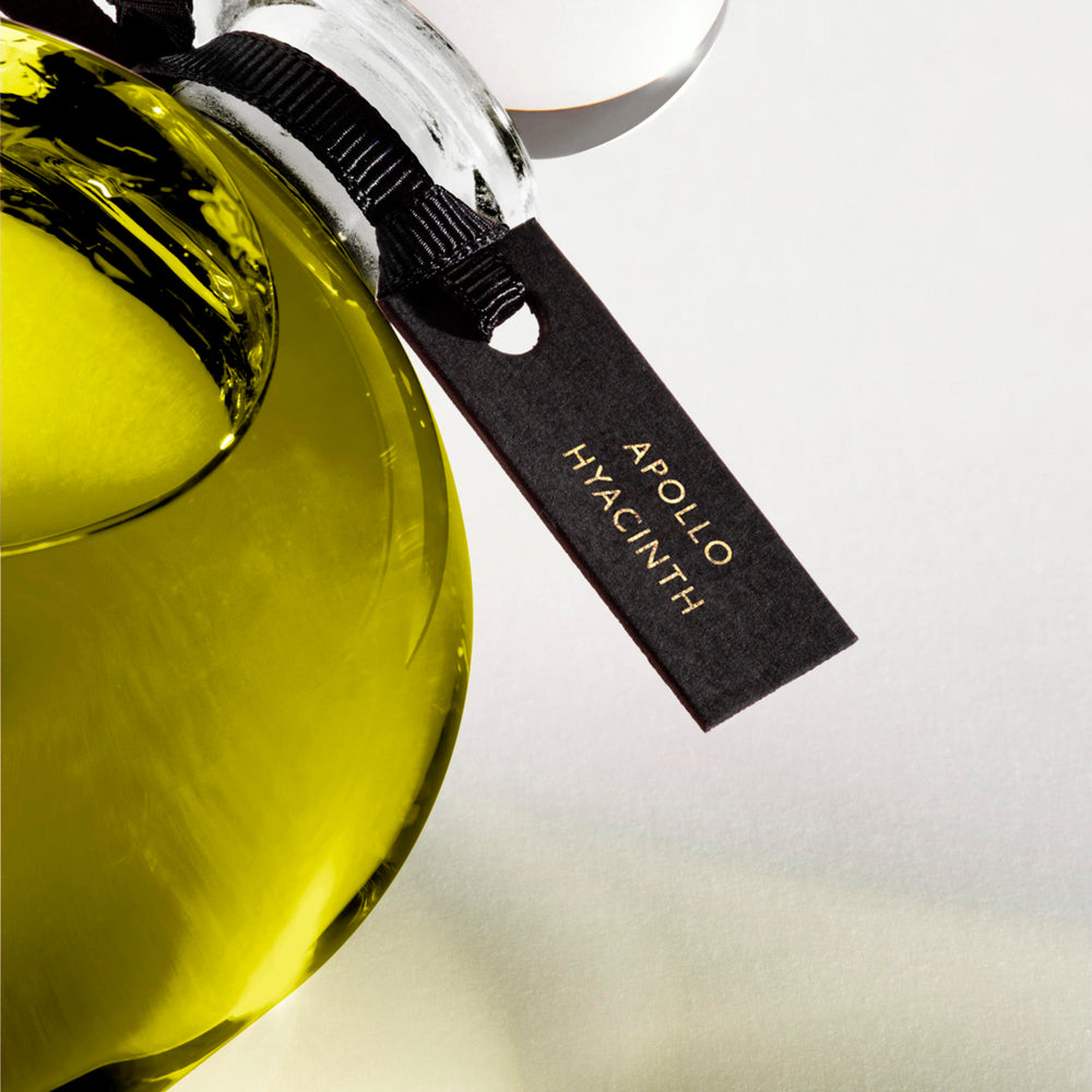 Detail of the top of the 250 ml bottle, with transparent glass and greenish perfum. Spherical cap with black ribbon. Apollo Hyacinth, a fragrance by Eric Butherbaugh.