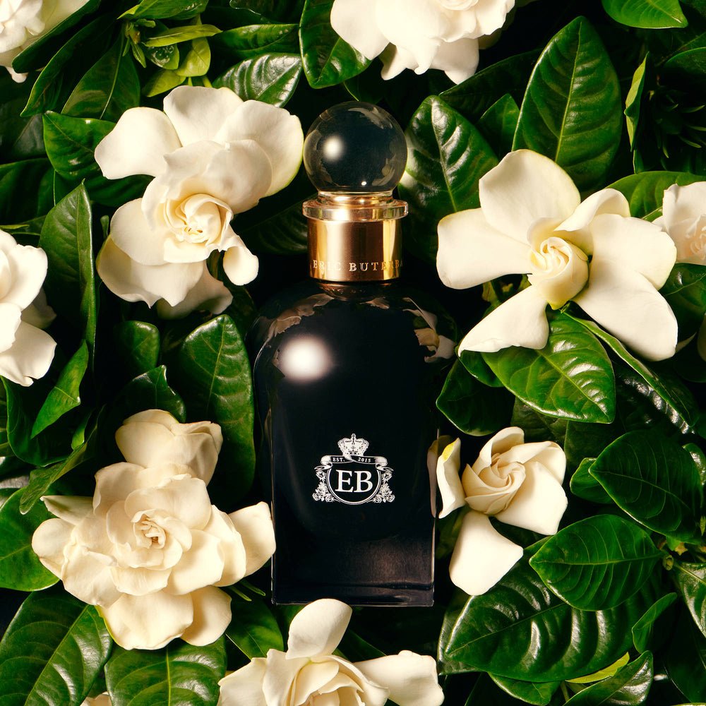 A 100 ml Oud Gardenia bottle lying on a bed of gardenias.